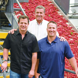 Three men standing in front of fruit conveyor belt