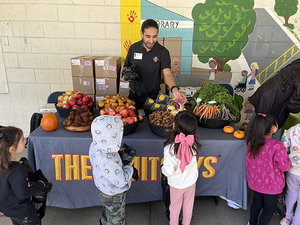 Man at school farmers market handing out fruit and vegetables to students